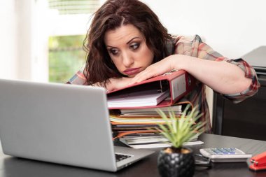 Masasında dosya yığını olan bitkin bir iş kadını.