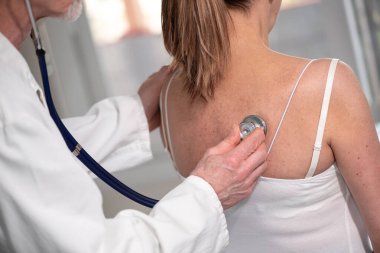 Doktor, kadın hastasına steteskopla bakıcılık yapıyor.