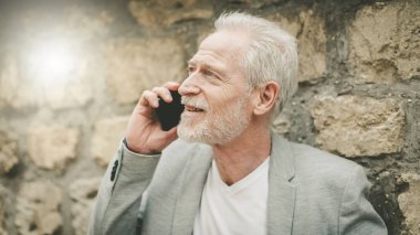 Olgun bir adam cep telefonunu açık havada kullanıyor.