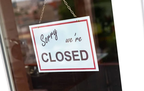 Sorry we\'re closed sign hanging behind a store window