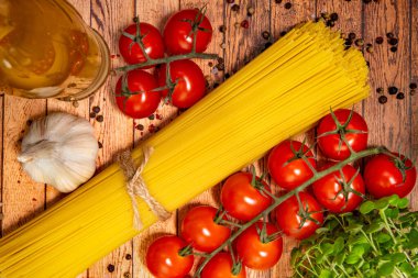 Masanın üzerinde spagetti, domates, ot, biber, zeytinyağı ve sarımsak var..