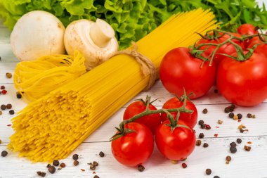 Masanın üzerinde spagetti, domates, ot, biber, sarımsak ve mantar var..