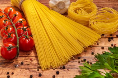 Masanın üzerinde spagetti, kiraz domatesleri, makarna, bitki, biber ve sarımsak var..