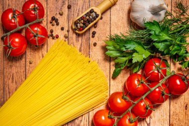 Masanın üzerinde spagetti, domates, dereotu, maydanoz, ahşap kepçe içinde biber ve sarımsak var..