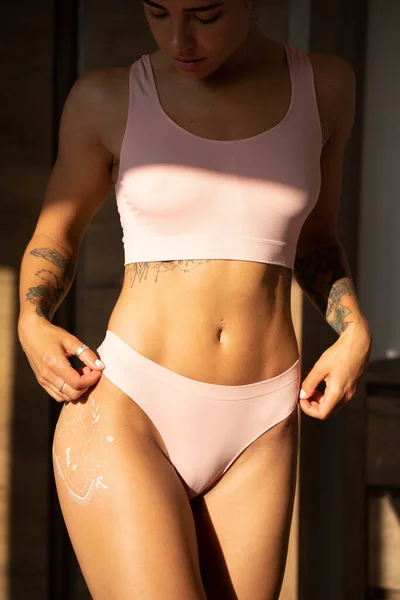 Beautiful sexy girl with sporty body posing in pink lingerie on wooden background. Women with tattoos in sporty underwear . Sport fashion style photo.