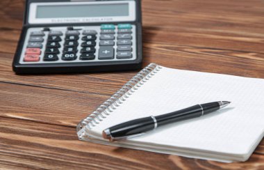 Bir doku ile kahverengi ahşap bir masa üzerinde bir hesap makinesi ve siyah kalem ile bir dizüstü bilgisayar vardır. Bir yazıt veya başlık için boş alan.