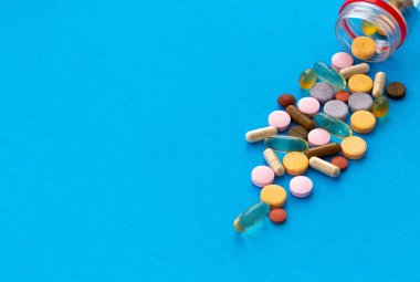 Kapsül ve tabletlerde çok renkli vitaminler bir şişeden dökülen, mavi bir arka plan üzerine. Kopyalama alanı.