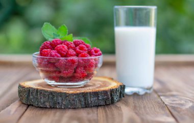 Yaz bahçesinde ahşap bir masada bir bardak süt ile ahşap bir stand üzerinde olgun ahududu bir fincan.