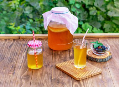 Kombucha ile iki bardak, ahşap kahverengi bir masada ahududu ve böğürtlen bir fincan ile bir yaz bahçesinde.
