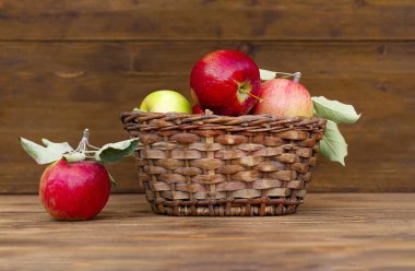 Elma hasat edin. Kahverengi arka planlı eski ahşap bir masa üzerinde hasır sepette kırmızı elma.