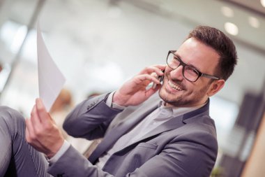 Smartphone kullanarak ve ofiste çalışırken gülümseyen genç işadamı