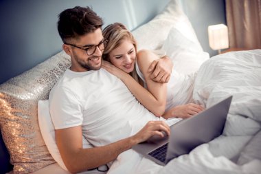 Yatakta yatan dizüstü bilgisayar ile genç Çift