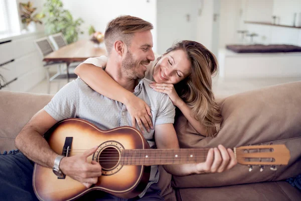 Pareja Joven Sentada Sofá Mientras Hombre Toca Guitarra Sala Estar —  Fotos de Stock