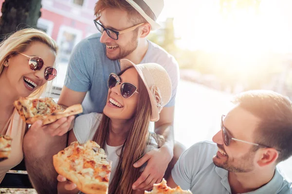 four young people eating pizza outdoor