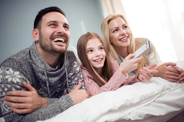 family watching television together and lying in bed at home