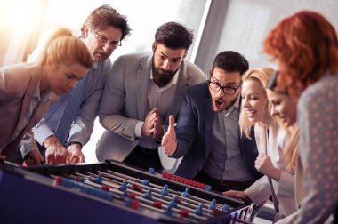 İş adamları birlikte harika vakit geçiriyorlar. Meslektaşlar modern ofiste masa futbolu oynuyorlar..