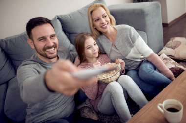 Mutlu aile - baba, anne ve kızı rahatlatıcı, Tv izlerken ve evde oturma odasında patlamış mısır yemek.