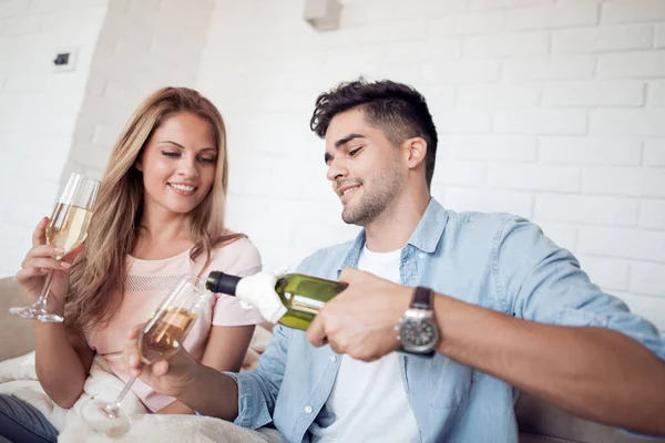 Loving relaxed young couple with wine glasses sitting in living room at home.Man pours wine into a glass.