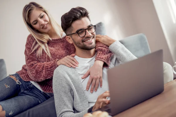 Mutlu çift gülüp, dizüstü bilgisayar kullanarak onların kanepede rahatlatıcı oturma odasında Anasayfa