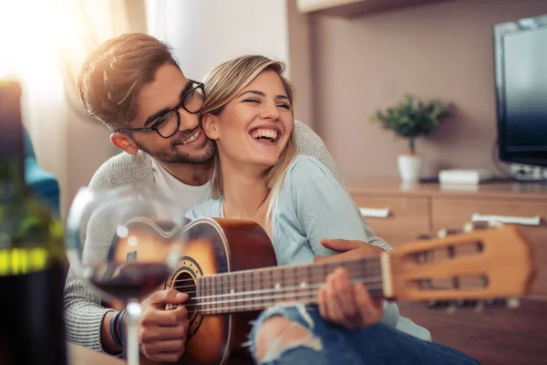 Man playing guitar in living room and woman listening,romantic moments.