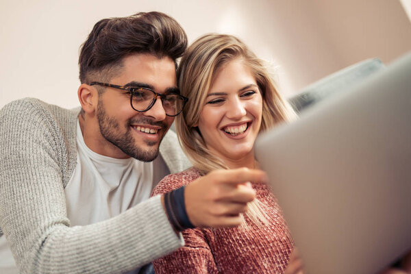 Happy couple relaxing on their couch using the laptop, smiling  at home in the living room