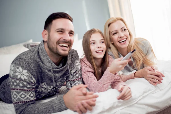 Adorable family watching television together,lying in bed at home. They are spend wonderful time together.