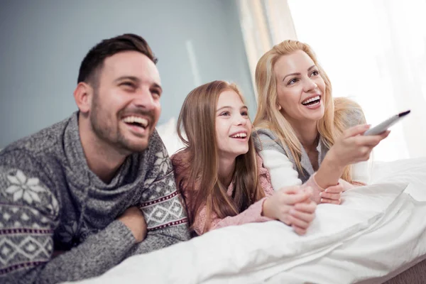 Adorable family watching television together in their bedroom.
