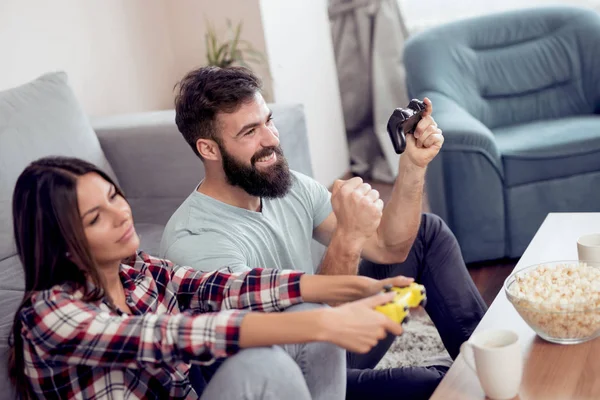 幸せなカップルの座っているコント ローラーを押しながら笑ってビデオ ゲームをプレイ — ストック写真