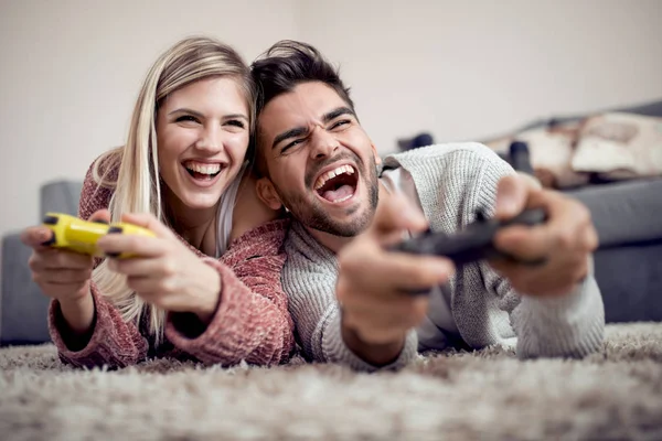 Cheerful couple playing video games while lying on a carpet.
