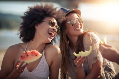 Sahilde eğleniyor ve karpuz yeme mutlu genç arkadaşlar.