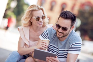 Kahve içme ve yaz aylarında şehir parkında oturan ve tablet bilgisayarı kullanan kadın ve erkek.