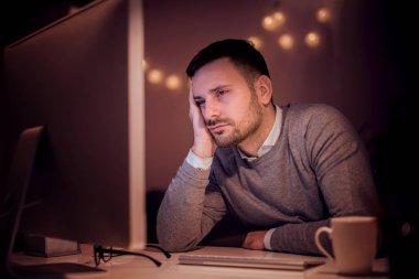 Gece geç saatlerde çalışan bir bilgisayar kullanarak, masada oturan genç adam, çok yorgun.