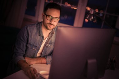 Gece geç saatlerde çalışan bir bilgisayar kullanılarak masada oturan genç adam.