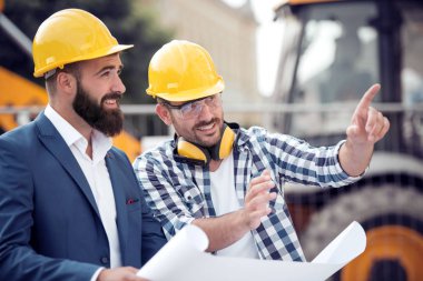 Mutlu Mühendisi Şantiye meslektaşı ile güneşli günde tartışıyor. Onlar oluşturmak için planlama.