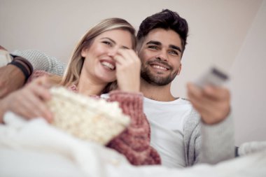 Mutlu genç çift kanepede evde patlamış mısır ile yalan ve Tv izlerken.
