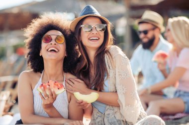 Sahilde eğleniyor ve karpuz yeme mutlu genç arkadaşlar.