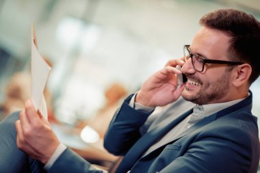 Akıllı telefon kullanarak ve ofiste çalışırken gülümseyen genç işadamı.