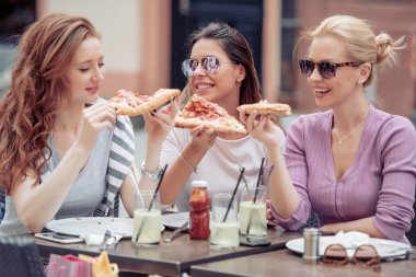 Üç neşeli kız açık bir kafede pizza yemek. İnsanlar, yemek, içmek ve yaşam tarzı kavramı.