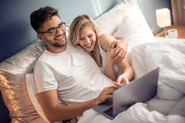 有笔记本电脑的年轻夫妇在床上 男人和女人喜欢看视频在笔记本电脑 而在卧室放松 — 图库照片