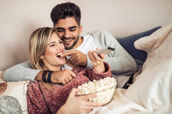 幸せな若いカップルは ポップコーンと自宅のソファに横になっているとテレビを見て — ストック写真