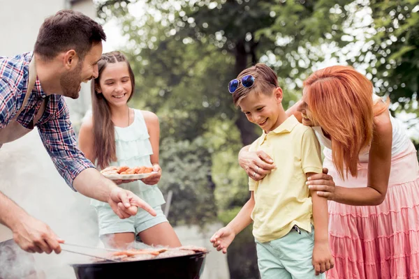 Leisure,food,people and holidays concept - man cooking meat on barbecue grill for his family at summer outdoor party.