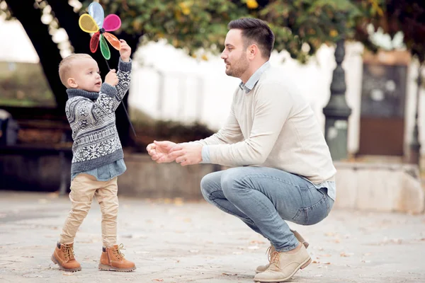 Küçük çocuk ve babası sokakta kağıt yel değirmeni ile oynarken. Aile, seyahat, tatil, babasının gün kavramı.