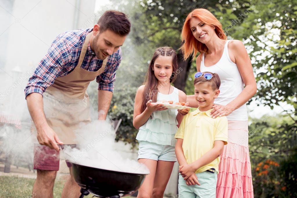 Leisure,food,people and holidays concept - man cooking meat on barbecue grill for his family at summer outdoor party.