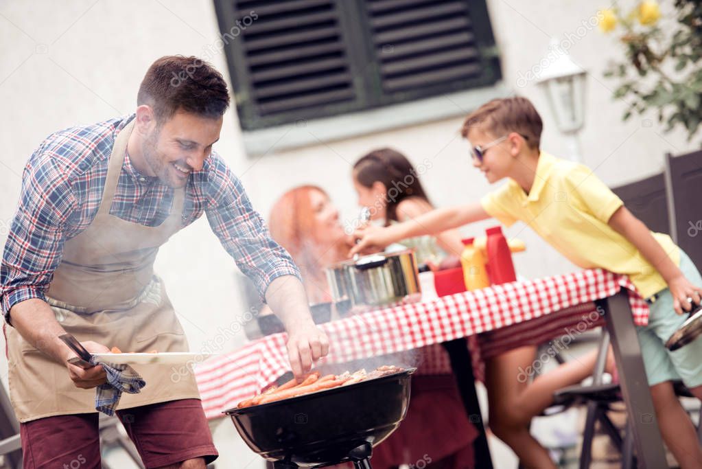 Leisure,food,people and holidays concept - man cooking meat on barbecue grill for his family at summer outdoor party.