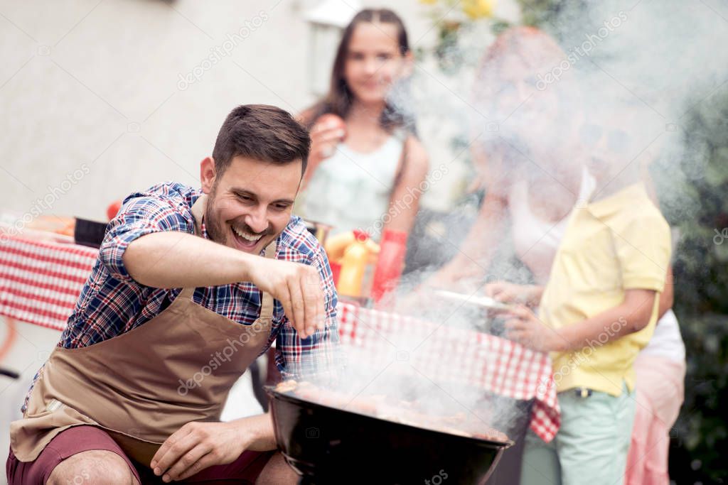 Leisure,food,people and holidays concept - man cooking meat on barbecue grill for his family at summer outdoor party.