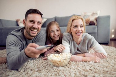 Baba, anne ve kızı yerde yatarken ve Tv izlerken.