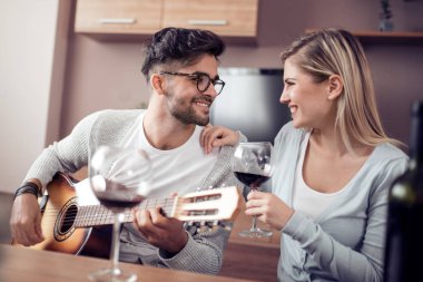 Mutlu genç çift birlikte masada akustik gitar ve kırmızı şarap ile dinlenme.
