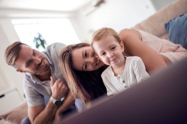 Evde koltukta oturan bir dizüstü bilgisayar kullanarak neşeli bir aile portresi.