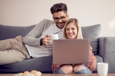 Koltukta oturan çift, ev kahve içmek ve laptop kullanma.