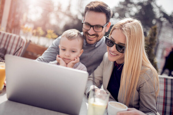 Happy young parents with their little boy in outdoors cafe.